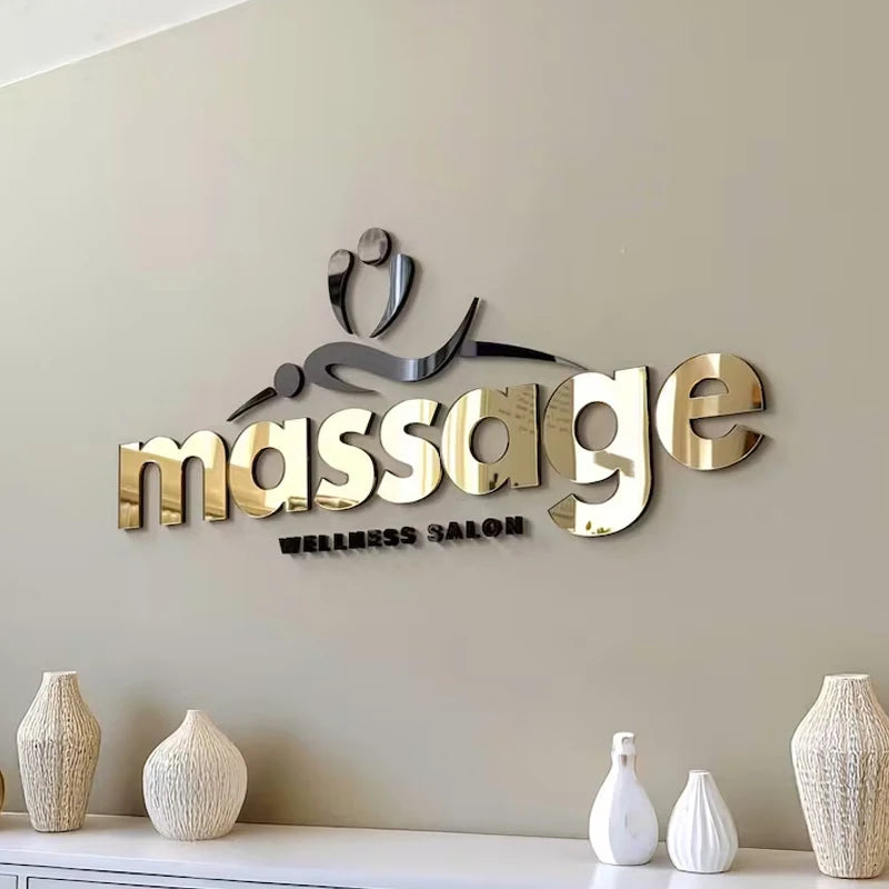3D metallic wall sign reading 'massage wellness salon' with a stylized massage therapist icon, mounted on a beige wall above a console table with decorative vases.