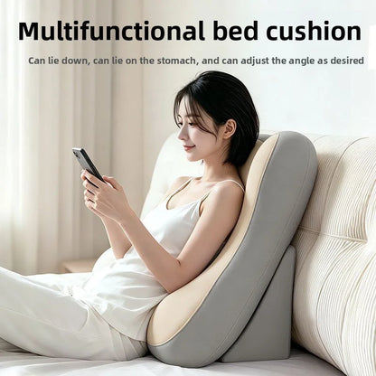 A woman in a white camisole and pants reclines on a gray and beige multifunctional bed cushion, holding a smartphone. The cushion is shown in a softly lit bedroom setting with text at the top reading 'Multifunctional bed cushion' and additional feature copy.