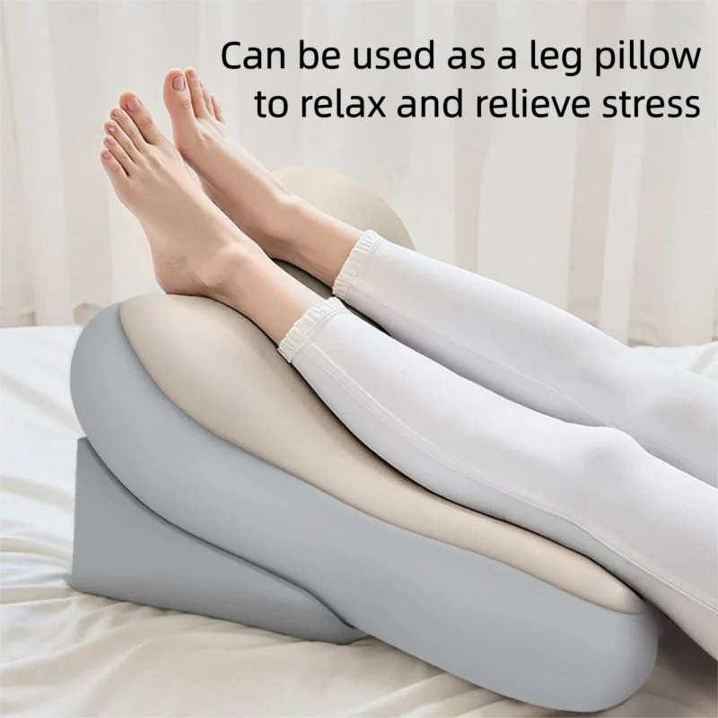 A curved contoured leg pillow in light gray and beige is shown on a bed with a person's legs resting on top, demonstrating its use as a leg pillow to relax and relieve stress.
