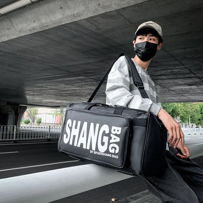 Person holding a black duffel bag with 'SHANG' branding under a bridge.