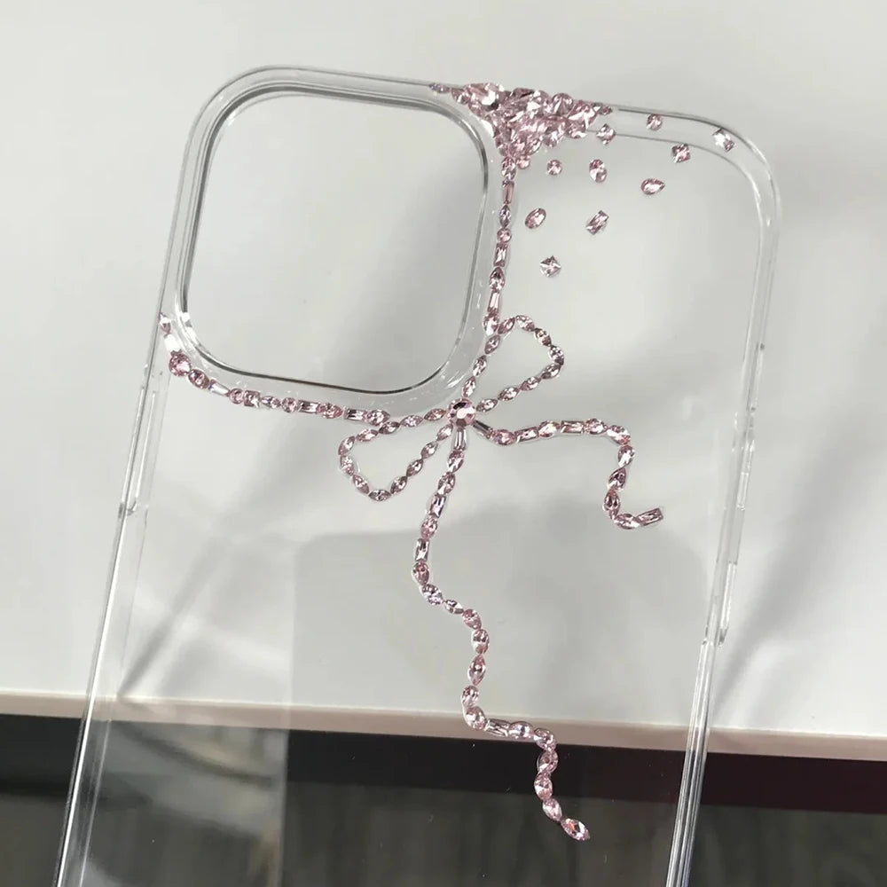 A clear phone case with a decorative pink rhinestone bow design, shown on a white surface.
