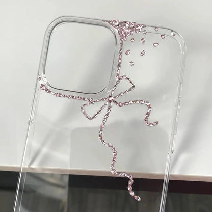 A clear phone case with a decorative pink rhinestone bow design, shown on a white surface.