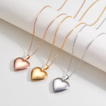 Three heart-shaped pendant necklaces on delicate chains, shown in rose gold, yellow gold, and silver finishes, arranged diagonally on a white background.