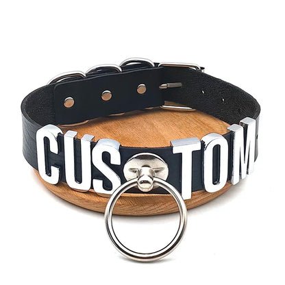 Black leather collar with metal rings and 'CUSTOM' letters on a wooden stand.