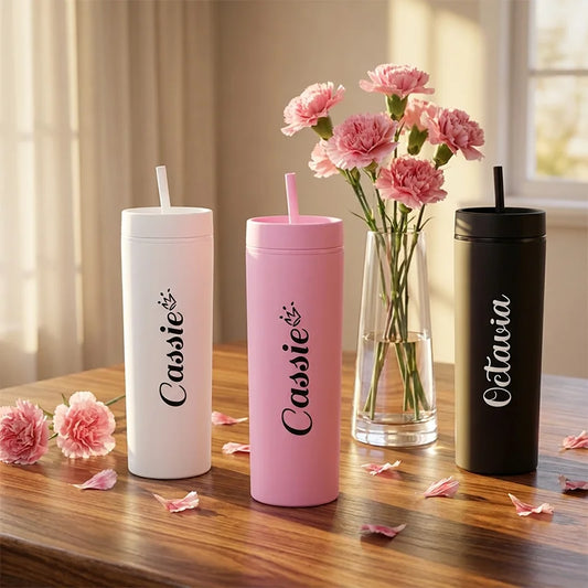Three personalized tumblers with names 'Cassie' and 'Eletavia' on a wooden table with pink flowers.