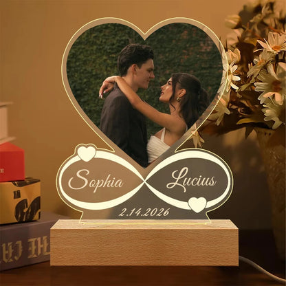 Heart-shaped photo frame with engraved names and date, placed on a surface with a blurred background.