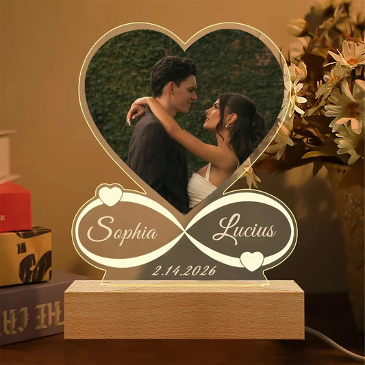 Heart-shaped photo frame with engraved names and date, placed on a surface with a blurred background.